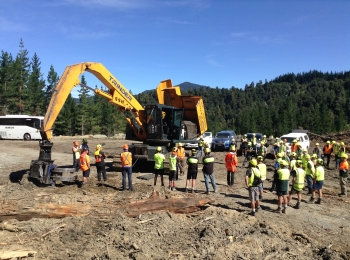 A group of people standing around a forest harvest machine