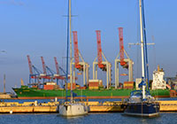 yachts docked with container ship in the background