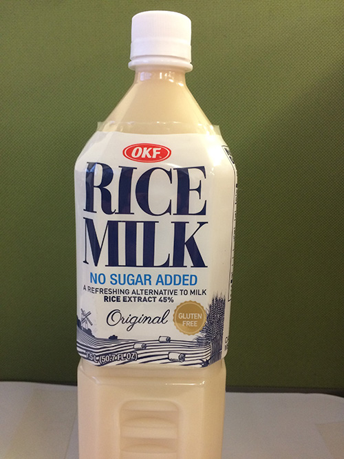 A closep image of an OFK plastic bottle of rice milk against a green background.