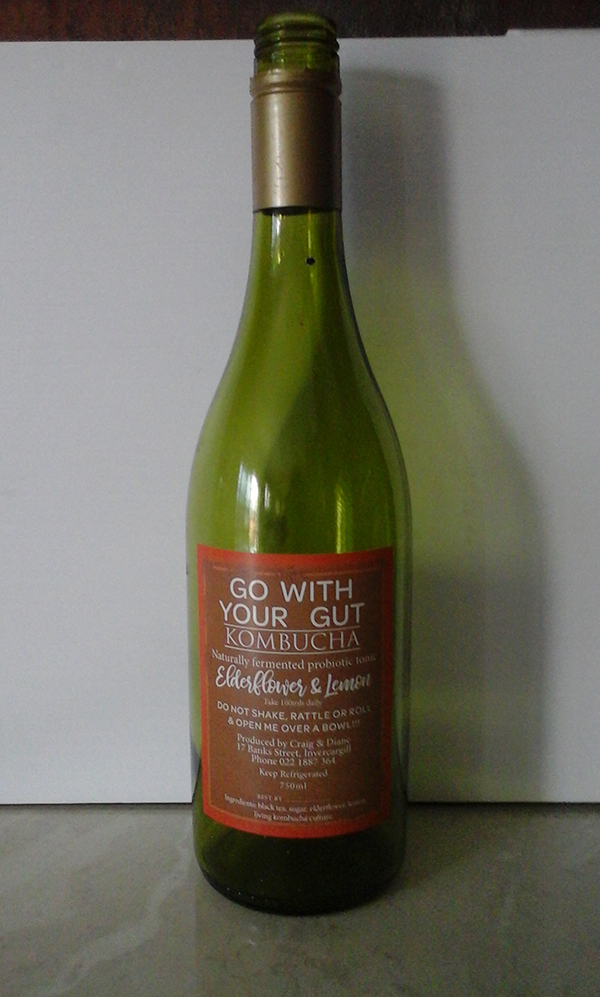 An empty glass bottle of kombucha with a label showing the elderflower and lemon favour
