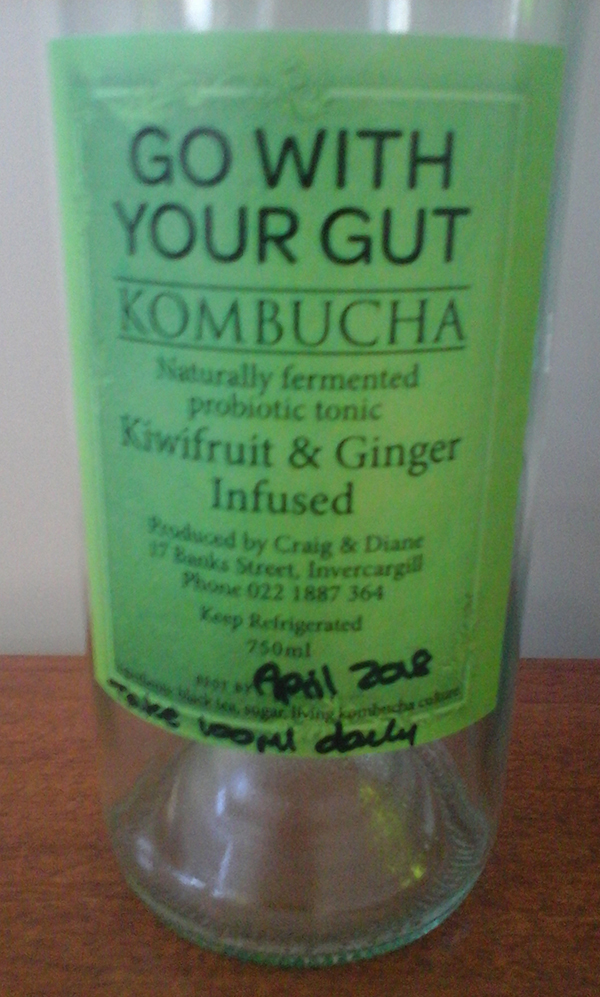An empty glass bottle of kombucha, kiwifruit and ginger flavour.