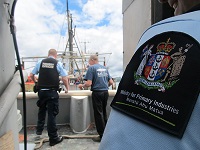 Three fishery officers on a fishing boat. A cloth MPI badge on the shirt sleeve of one of the officers is in the foreground.