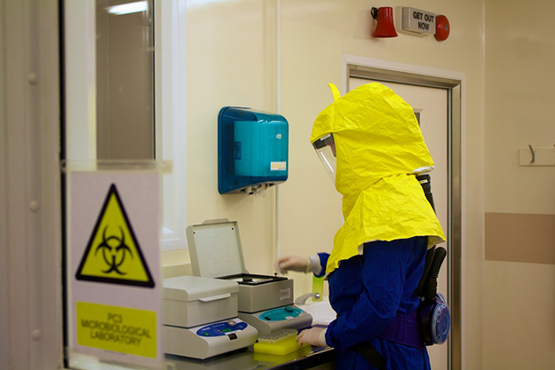A lab worker wearing protective head gear and gloves, prepares a sample.